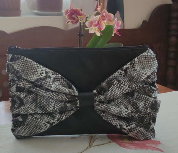 Fekete műbőr cipzáros táska fehér-fekete kígyómintás textilbőr masnival és fekete béléssel